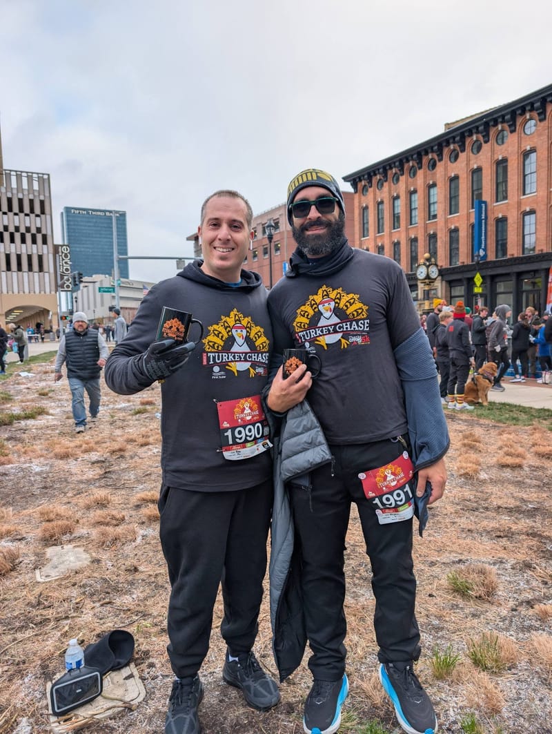 Two runners in matching event shirts and numbered bibs standing on frozen ground downtown, dressed for cold.