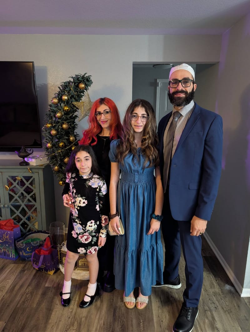 Abe with his wife and two daughters at home, dressed up, a lit Christmas tree behind them.