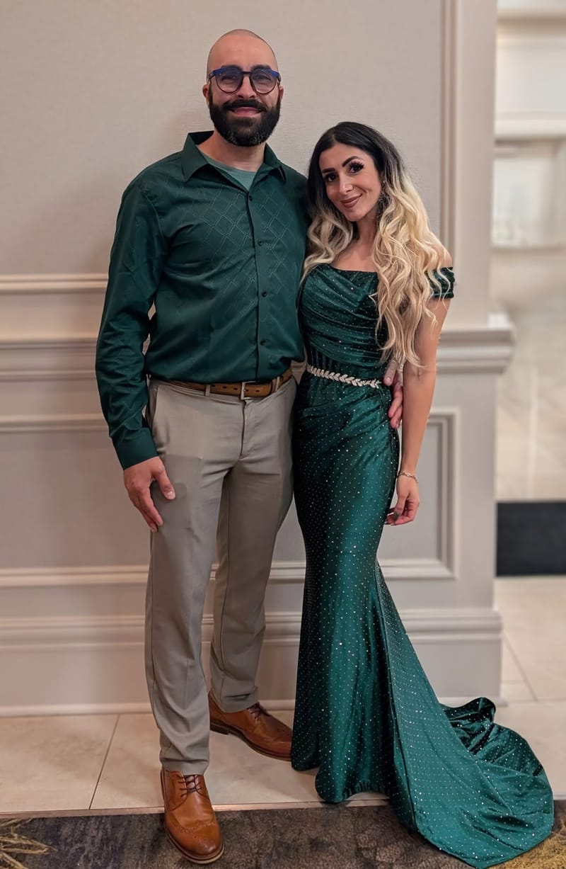 Abe in a dark green shirt beside his wife in a long emerald gown, dressed for an evening out.