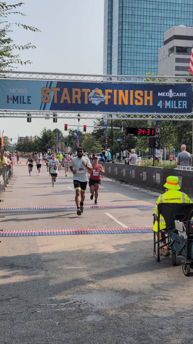 A start and finish gantry across a city street with runners approaching and the Toledo skyline behind.