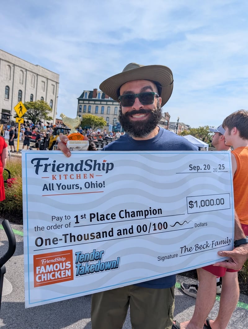 Abe in a wide-brimmed hat holding an oversized novelty check for one thousand dollars made out to First Place Champion, a gold chicken trophy in his other hand.