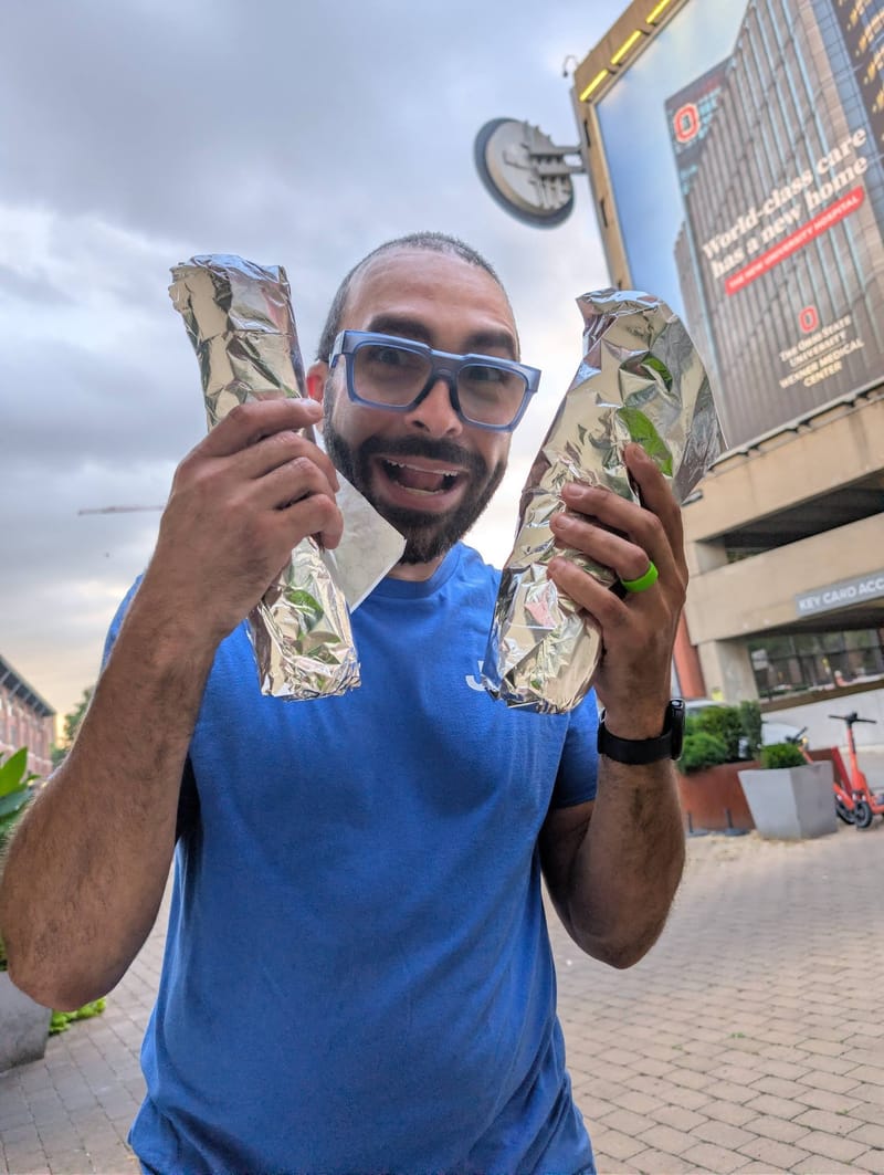Abe outdoors holding a foil-wrapped burrito in each raised hand, one per fist.