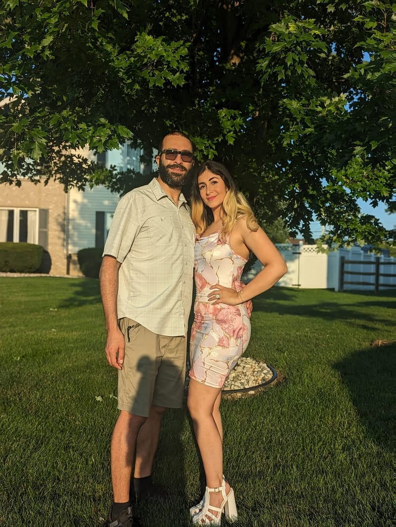 Abe and his wife standing together on grass under a broad shade tree in summer.