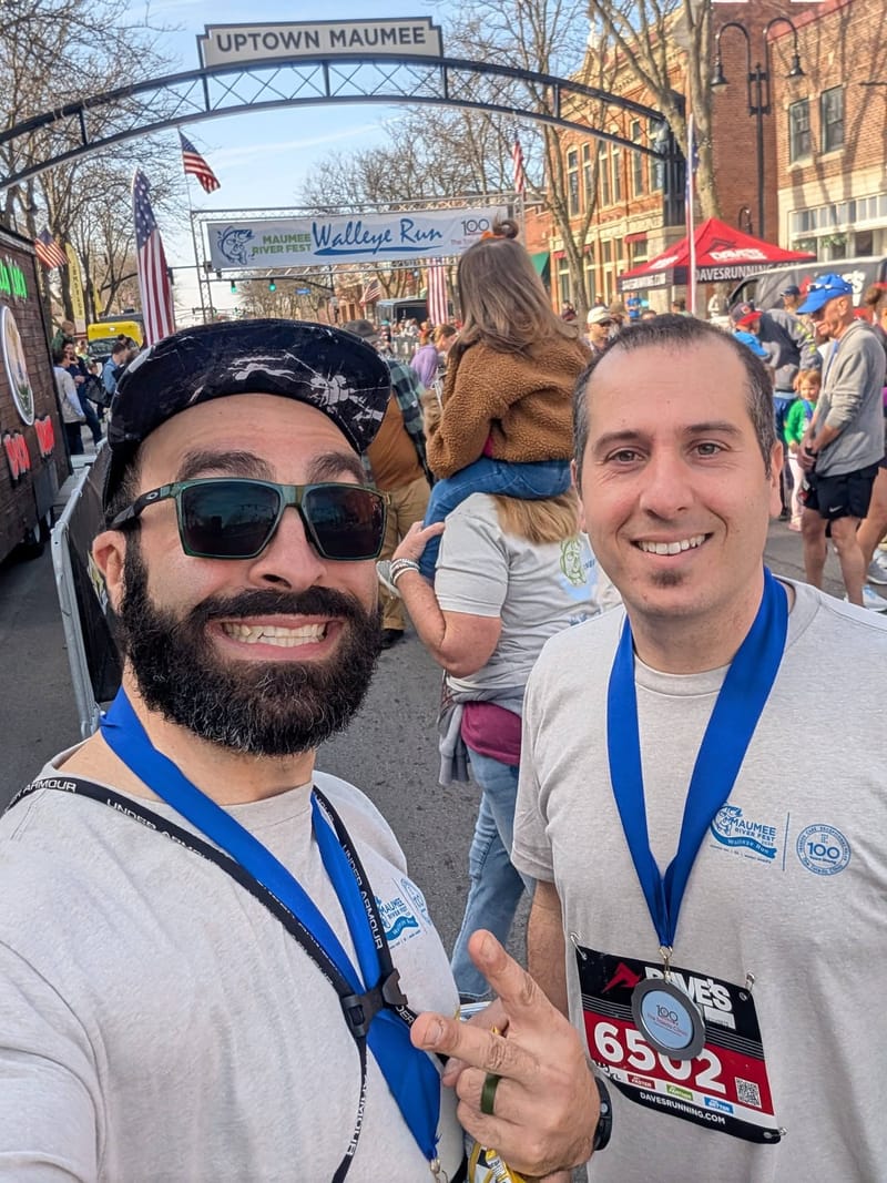Abe and another runner grinning with finisher medals under an Uptown Maumee arch.